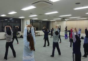 大会議室の広い空間で前に立つ講師に合わせてエクササイズを行う参加者の画像
