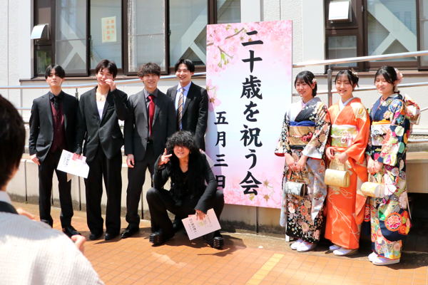 看板の前で記念撮影をする二十歳を祝う会の出席者の画像
